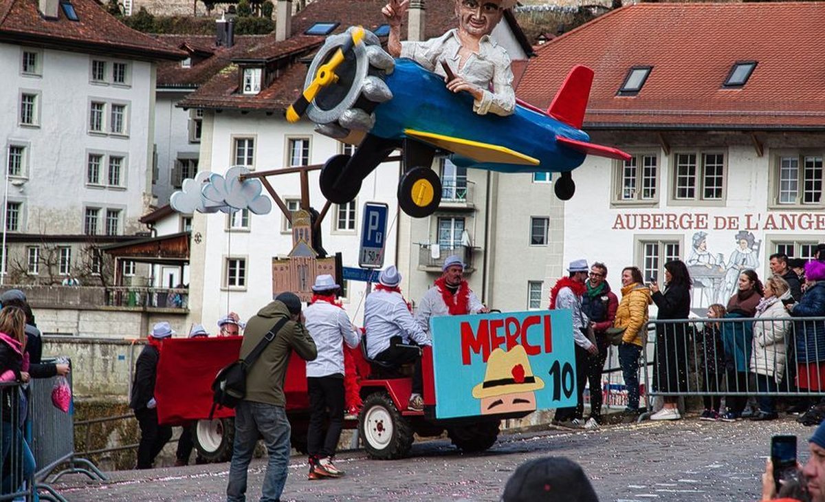 Char du Carnaval des Bolzes avec un avion bleu et un personnage géant devant l'Auberge de l'Ange, dans la Basse-Ville de Fribourg