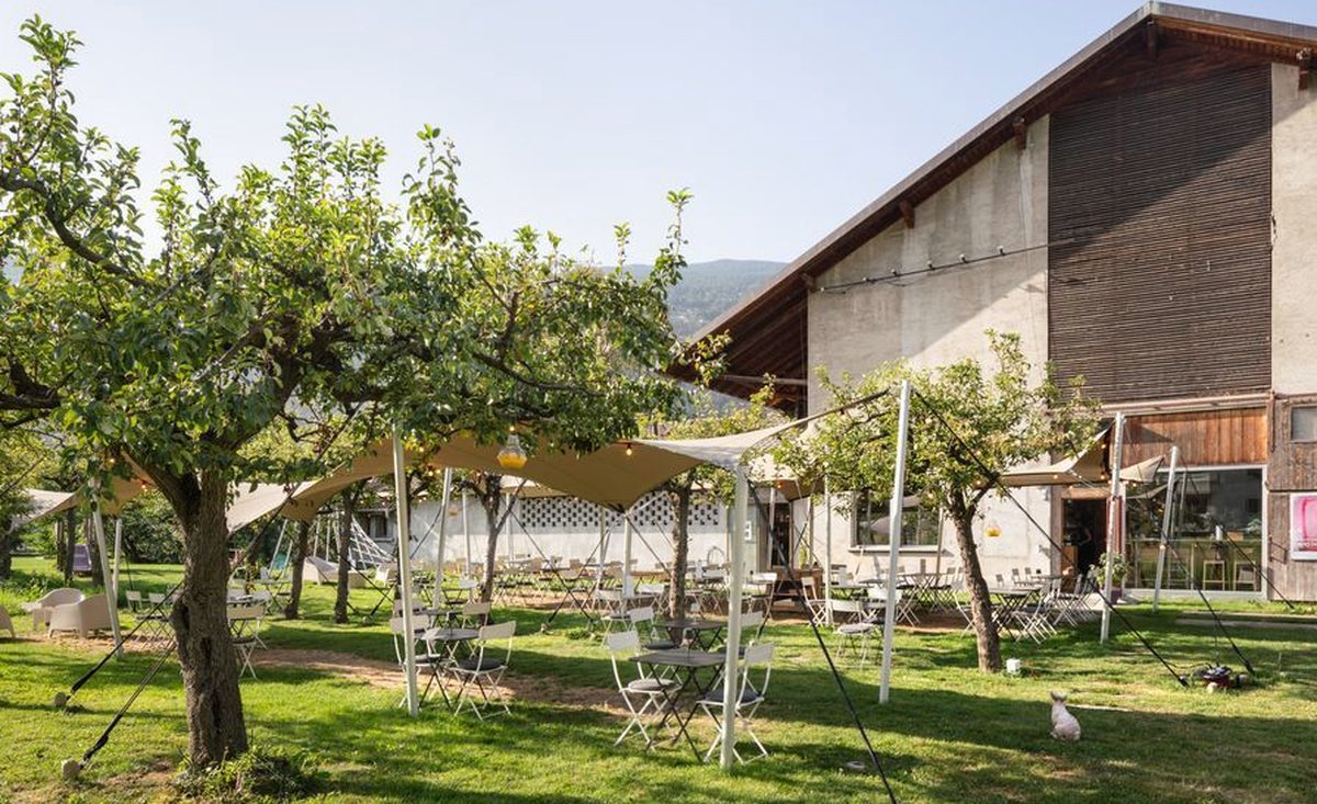 Tables et chaises sous les arbres fruitiers devant la grange de la Ferme-Asile à Sion
