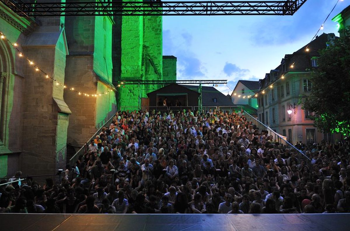 Public assis sur les gradins devant la cathédrale de Lausanne éclairée pendant le Festival de la Cité