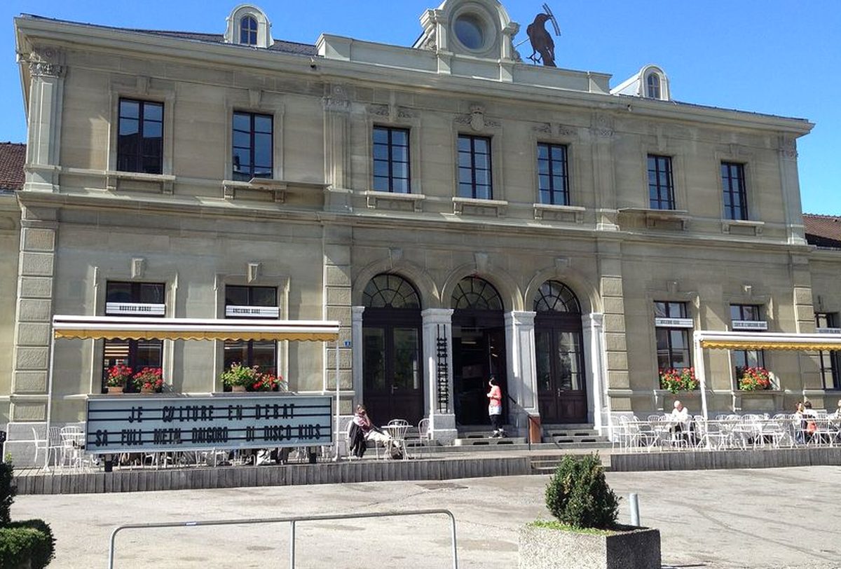Façade de l'Ancienne Gare de Fribourg avec la terrasse du Nouveau Monde et son panneau de programme