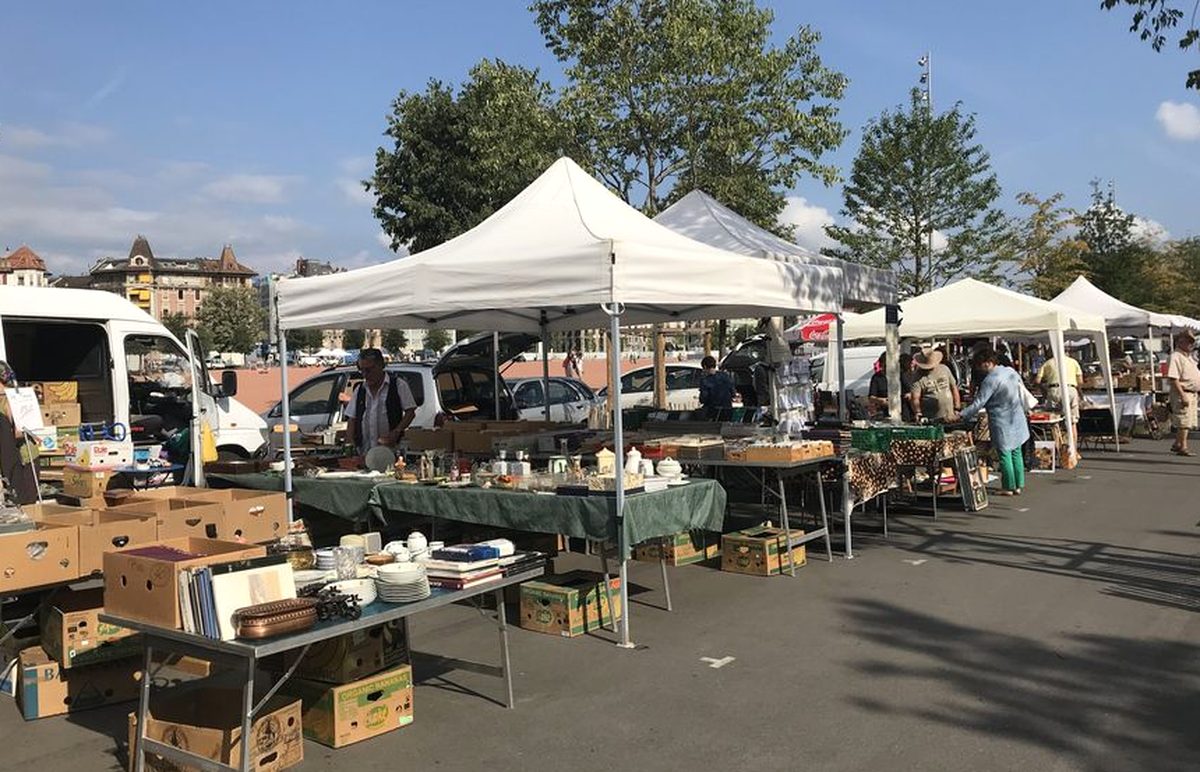 Stands sous tentes blanches du marché aux puces de Plainpalais à Genève, cartons de livres et vaisselle au premier plan