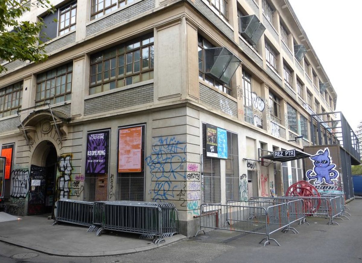Façade de L'Usine à Genève, entrée voûtée couverte de graffitis, affiches de concerts et enseigne Rez PTR